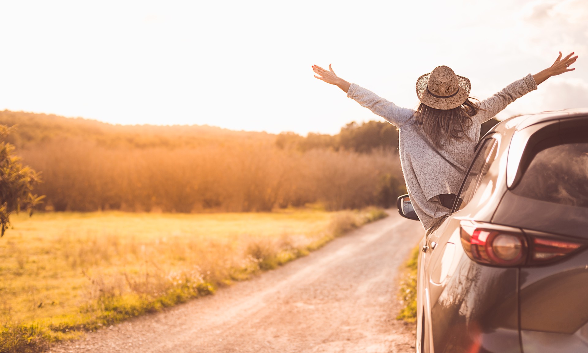 Happy girl celebrating success at sunset. The girl is wearing a hat and her arms are outstretched.